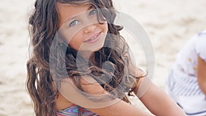 Close-up portrait of a pretty little Hispanic girl with waving in the wind long hair sitting on the beach.