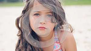 Close-up portrait of a pretty little Hispanic girl with waving in the wind long hair sitting on the beach.