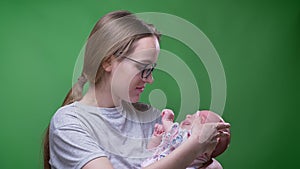 Close-up portrait of pretty mother holding and kissing her cute and beautiful newborn daughter on green background.