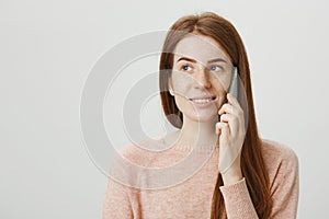 Close-up portrait of pretty redhead woman holding gadget near ear, waiting for somebody to pick up phone, looking aside