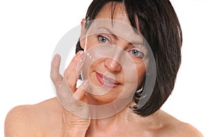 Close up portrait of pretty senior woman using face cream