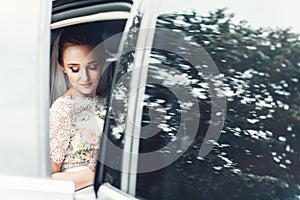 Close-up portrait of a pretty shy bride in a car window