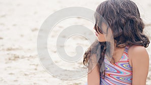 Close-up portrait of a pretty little Hispanic girl with waving in the wind long hair sitting on the beach.