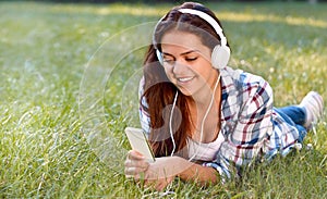 Close up portrait of pretty young girl listening music lying at the grass