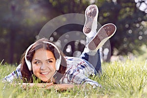 Close up portrait of Pretty young girl listening music lying at the grass