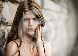 Close-up portrait of a pretty young white woman, standings against a rough wall