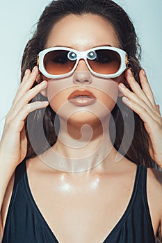 Close up portrait of pretty young woman with white glasses in luxury black bikini. Female fashion model posing with sunglasses.