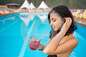 Close-up of portrait profile young brunette woman holding a cocktail on a blurred background of resort swimming pool