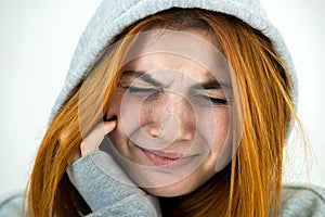 Close up portrait of sad depressed young redhead woman wearing warm hoodie pullover