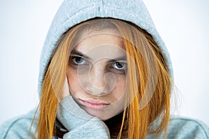 Close up portrait of sad depressed young redhead woman wearing warm hoodie pullover