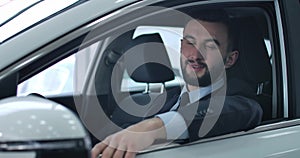 Close-up portrait of satisfied Caucasian young man posing in car on driver`s seat. Positive handsome man buying new