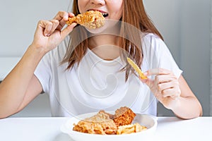 Close up portrait of a satisfied pretty Asian woman eating fried chicken and french fries isolated over white background.