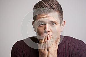 Close up portrait of a scared young man with hands to face