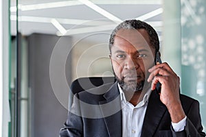 Close-up portrait of a senior African-American man sitting at a desk in the office, talking on the phone and looking