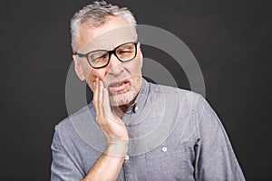 Close-up portrait of senior aged man suffering from toothache on black background