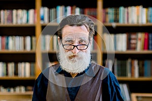 Close up portrait of senior man with beard and eyeglasses, looking at camera, standing on book shop market background