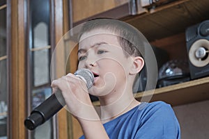 Close-up portrait of serious Asian boy holding microphone singing song karaoke at home concert.