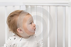 Close up portrait of a serious baby sitting in a white crib