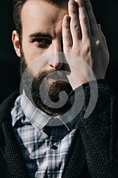 Close-up portrait of a serious bearded man with closed eye over black background