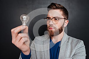 Serious bearded young man standing and looking at light bulb