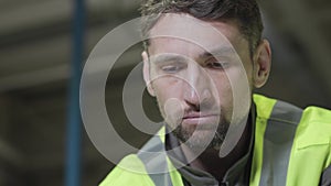 Close-up portrait of serious Caucasian man in green vest looking down. Professional worker working at manufacture plant