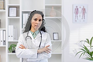 Close-up portrait of serious and confident hispanic female doctor, woman looking at camera with crossed arms