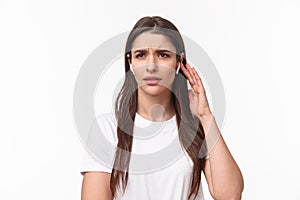 Close-up portrait of serious displeased young woman having troubles with using wireless earphone, have bad quality of