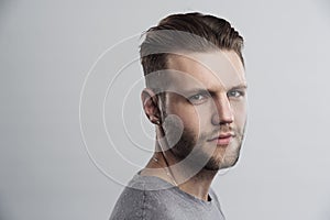 Close up portrait of serious gloomy bearded man with stylish hairstyle posing against white background. Handsome guy