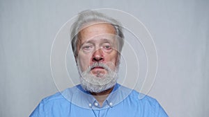 Close-up portrait of serious gray-haired mature man unemotionally looking at camera standing on white isolated