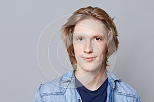 Close up portrait of serious handsome man with trendy hairdo, dark eyes, wears denim jacket, looks directly into camera, isolated