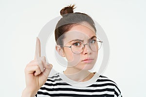 Close up portrait of serious woman in glasses, frowning and looking concerned, pointing finge rup, showing advertisement photo