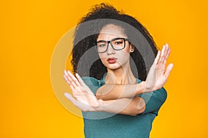 Close up portrait of a serious young african american woman showing stop or no gesture with her palm isolated over yellow