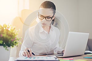 Close up portrait of serious young business lady economist in formal wear and with glasses, pony ail, concentrated on paper work