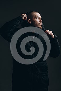 Close-up portrait of a serious young man in a jacket looking to the side on a gray background. bald with a beard