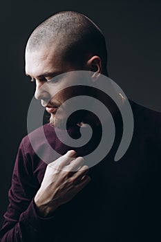 Close-up portrait of a serious young man looking away on a gray background. bald with a beard