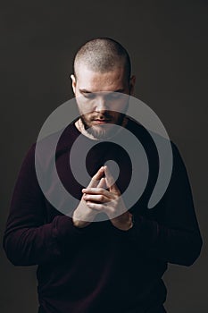 Close-up portrait of a serious young man looking down on gray background. bald with a beard