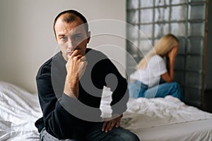 Close-up portrait of serious young man pensive looking at camera not talking after dispute with sad wife sitting apart