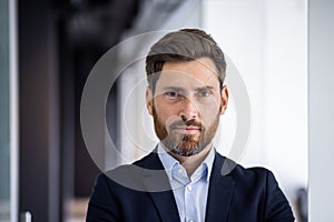 Close-up portrait of a serious young successful male businessman standing in the office in a suit and confidently