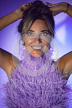 close-up portrait of a sexy woman in a purple dress with feathers sitting on a chair in a studio on a cycloram. eyes up