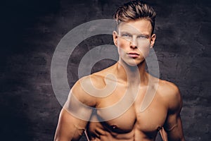Close-up portrait of a shirtless young man model with a muscular body and stylish haircut posing at a studio