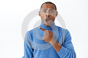 Close-up portrait of shocked and disappointed african american man complaining on something bad, pointing finger left