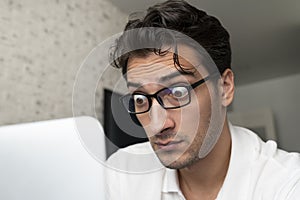 Close up portrait of shocked man with bugged eyes looking at laptop