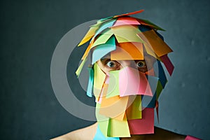 Close up portrait of shocked man with colorful sticky notes all over his face over gray background