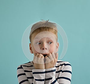 Close up portrait of shocked scare surprised young boy of nine years old, eyes wide open, isolated on blue background.