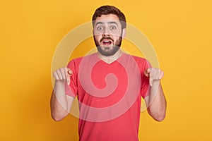 Close up portrait of shocked scared young male being afraid of something, pointing down with his fore fingers, having surprised