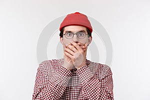 Close-up portrait of shocked young man heard something unbelievable and shook, close mouth with hands stare at camera as