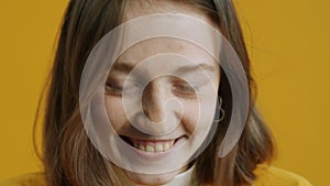 Close-up portrait of shy girl smiling looking at camera with modesty on yellow background