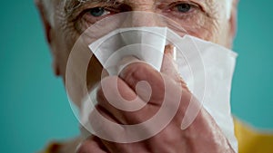 Close-up portrait of a sick elderly man wiping his nose with a napkin, suffering from a runny nose. Old man in Blue