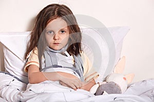 Close up portrait of sick girl in hospital bed, looking at camera, having upset look, feels unwel, taking temperature, laying in