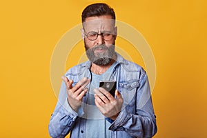 Close up portrait of single handsome Caucasian middle aged man in casual T shirt and denim jacket, texting using smartphone and